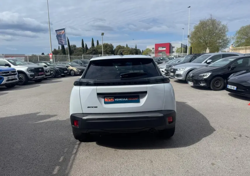 Vue arrière d’un Peugeot 2008 blanc 2024 avec feux noirs et lunette teintée, stationné en extérieur parmi d’autres véhicules.