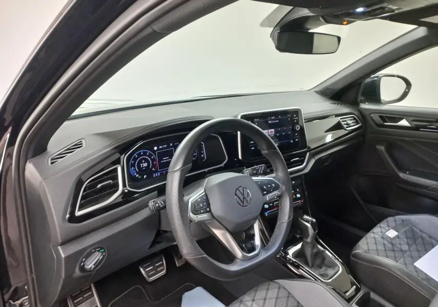 Vue intérieure côté conducteur du Volkswagen T-Roc 2025, tableau de bord numérique et volant multifonction en cuir noir.