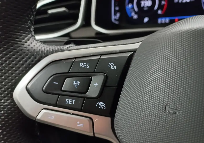 Gros plan sur les commandes du régulateur de vitesse au volant perforé d’un Volkswagen T-Roc 2025 finition R-Line.