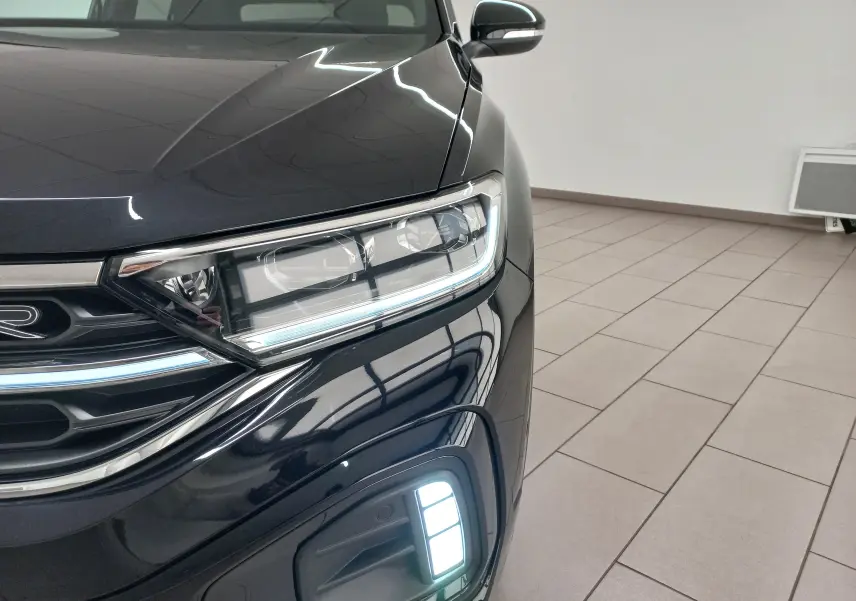 Gros plan sur l'avant droit du Volkswagen T-Roc 2025 noir intense nacré avec projecteurs Matrix LED allumés.