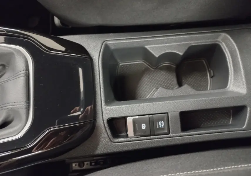 Gros plan sur la console centrale noire du Volkswagen T-Roc 2025, avec porte-gobelets et boutons frein à main électronique et Auto Hold.