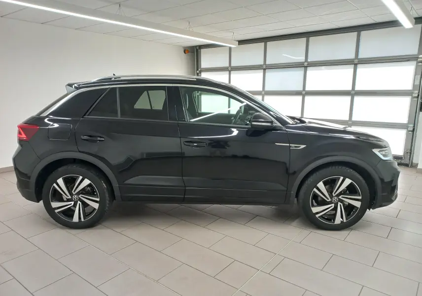 Vue de profil côté gauche du Volkswagen T-Roc 1.5 TSI 150 DSG7 R-Line en noir intense nacré, avec jantes distinctives et lignes dynamiques.