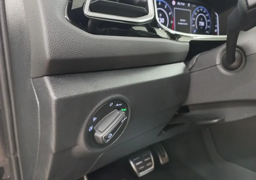 Détail du tableau de bord côté gauche du Volkswagen T-Roc 2025 noir intense, avec commande des phares et pédales en aluminium.