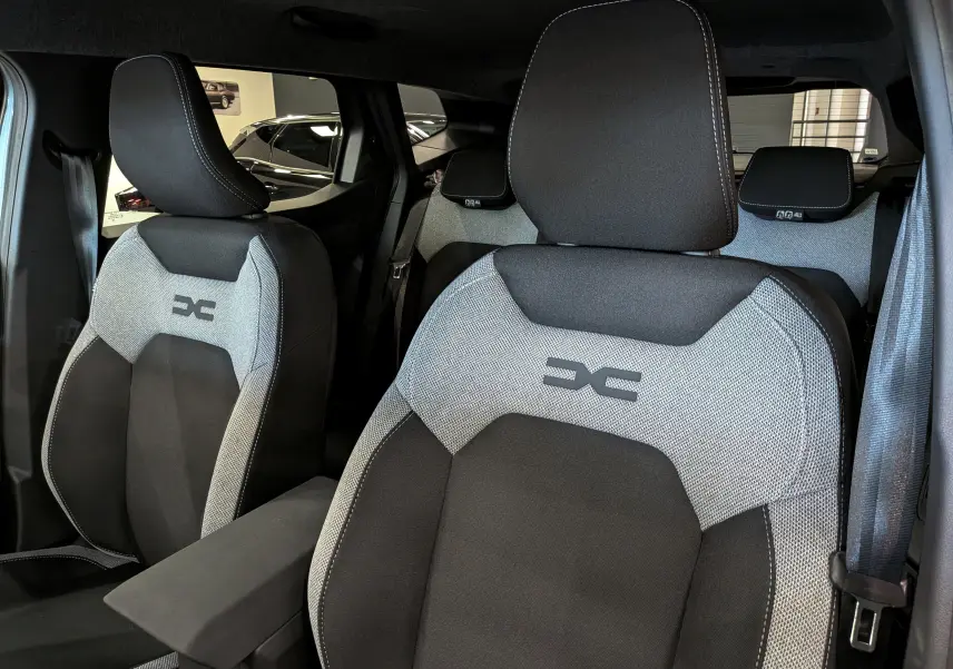 Vue intérieure rapprochée des sièges avant gris et noir avec logo Dacia sur un Duster Hybrid-G 2026.