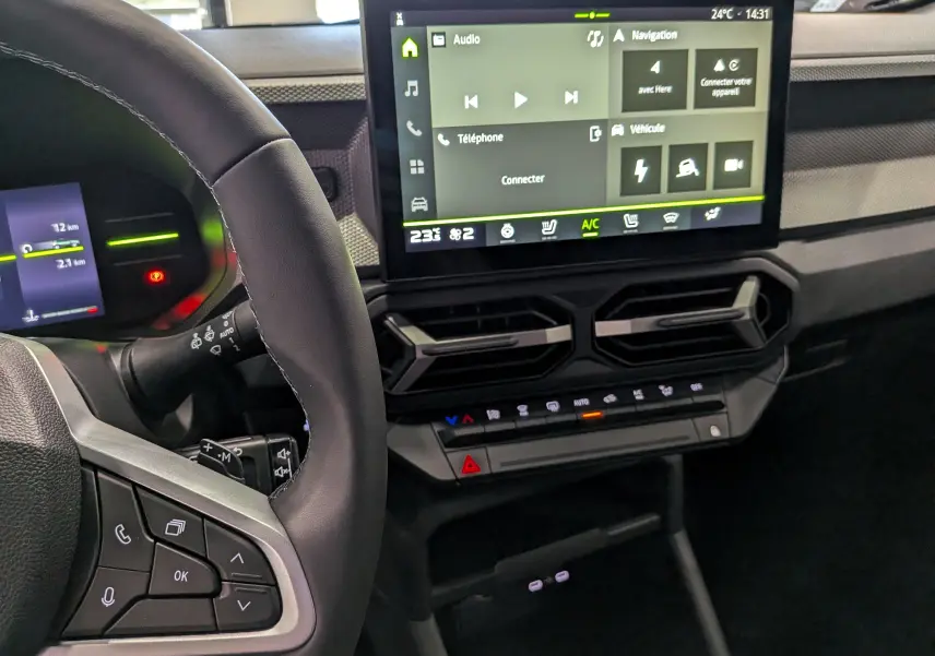 Vue intérieure centrée sur le tableau de bord et l'écran tactile du Dacia Duster Hybrid-G 150 CH 4x4, volant partiellement visible.