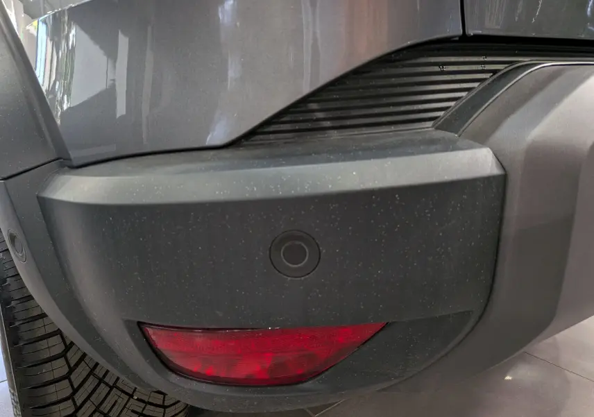 Gros plan sur le pare-chocs arrière droit gris schiste du Dacia Duster Hybrid-G 150 CH 4x4 avec feu rouge et capteur de recul.