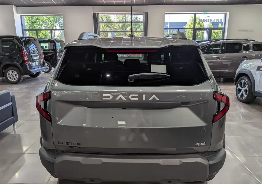 Vue arrière d'un Dacia Duster gris schiste hybride 4x4 en showroom, avec logo et feux arrière distinctifs.