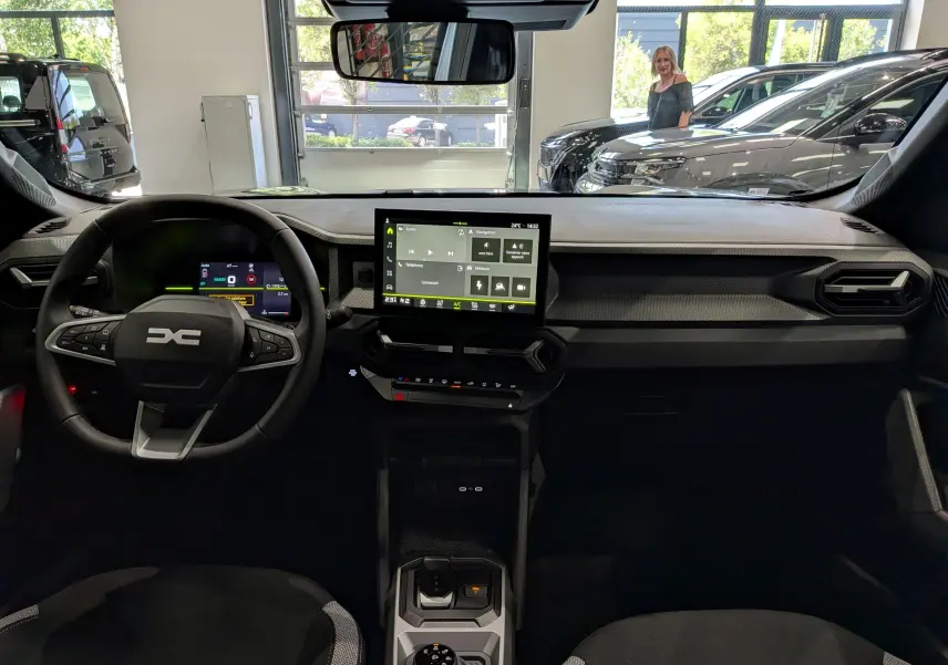 Vue intérieure avant du Dacia Duster Hybrid-G 150 CH 4x4 gris, avec tableau de bord numérique et écran tactile central.