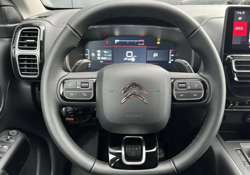 Vue intérieure centrée sur le volant noir cuir du Citroën C5 Aircross 2025 avec tableau de bord numérique et écran tactile.