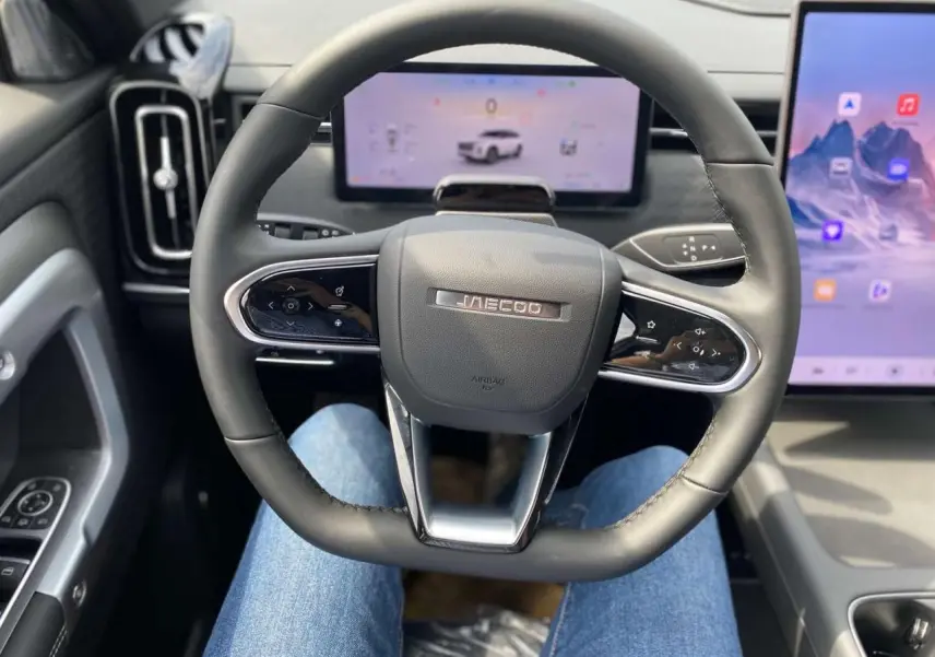 Vue intérieure centrée sur le volant JAECOO avec tableau de bord numérique et écran tactile latéral.