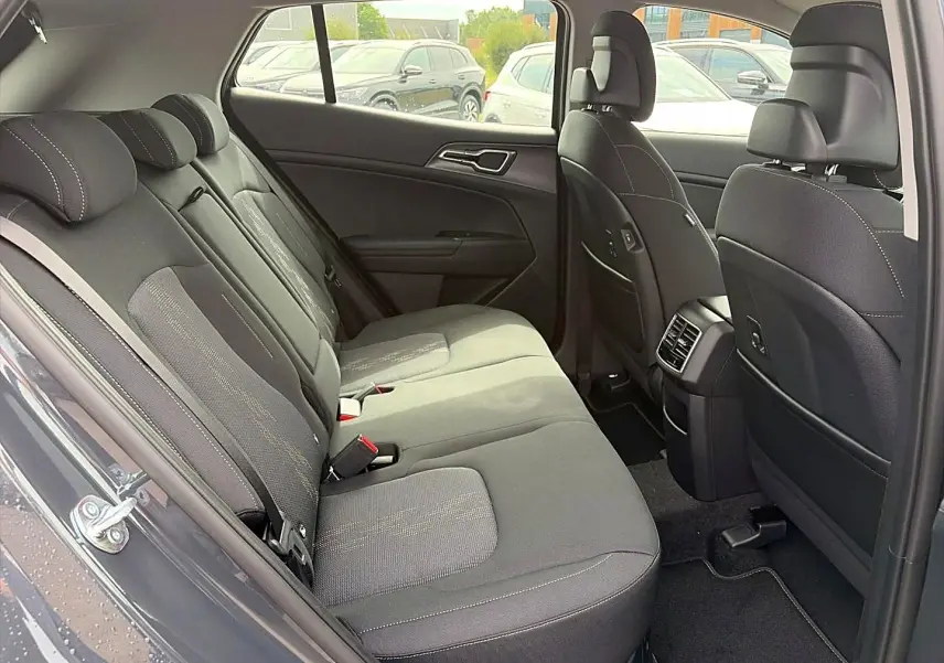 Vue intérieure côté gauche montrant la banquette arrière grise du Kia Sportage 1.6 hybride 239 active avec appuie-têtes et aérateurs centraux.