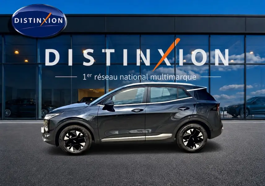 Profil côté gauche du KIA SPORTAGE 1.6 hybride 239 gris eclipse devant une vitrine avec logo Distinxion.