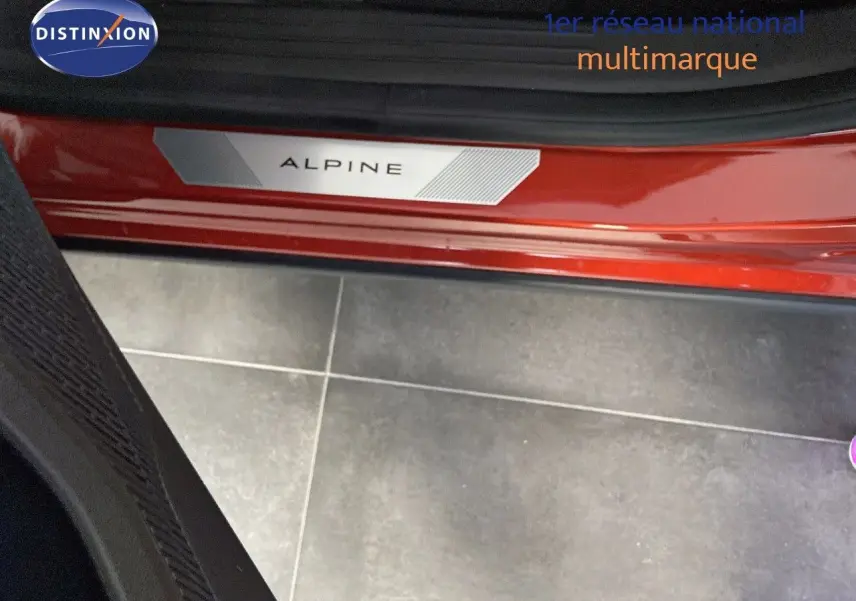 Gros plan sur la plaque Alpine rouge flamme métal visible à l'entrée côté gauche de la Renault Rafale 2024.