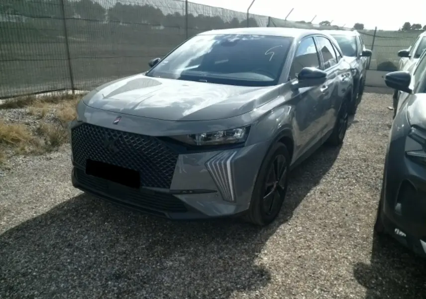 DS7 1.6 E-Tense gris laqué en 3/4 avant droit, avec calandre noire et feux LED distinctifs en forme de griffes.