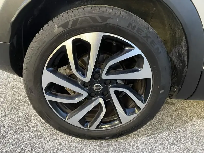 Gros plan sur la roue avant gauche de l'Opel Grandland X blanc avec jante alliage bicolore et pneu Nexen visible.