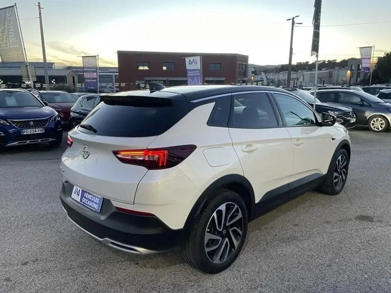 Opel Grandland X blanc avec toit noir, vue 3/4 arrière droit, feux arrière allumés, jantes alliage distinctives.