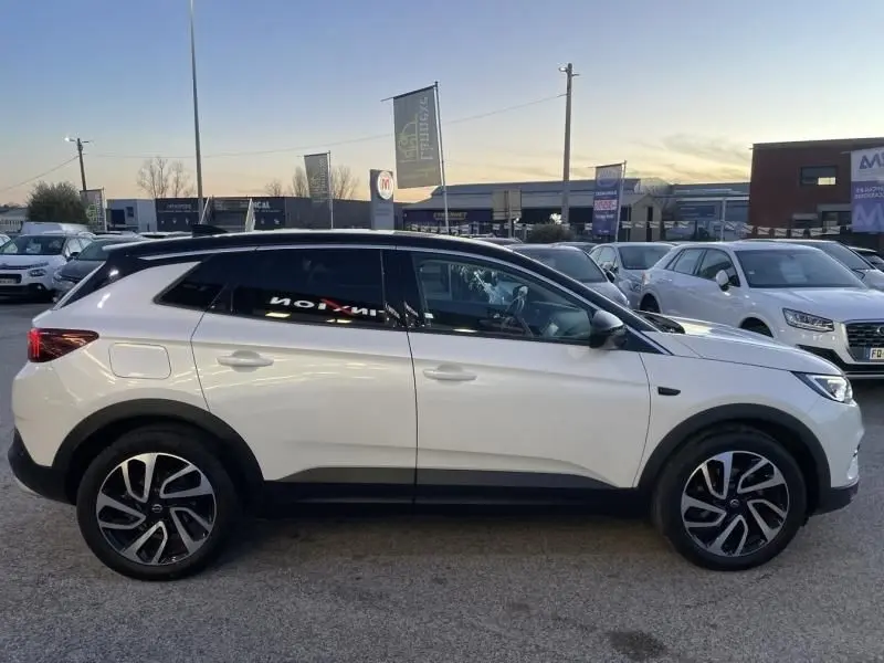 Vue de profil côté gauche d’un Opel Grandland X blanc avec toit noir, jantes alliage et vitres teintées, en extérieur.