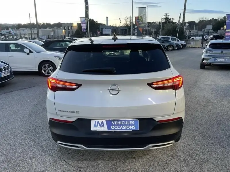Vue arrière d'un Opel Grandland X blanc avec toit noir, feux allumés, sur un parking extérieur en fin de journée.