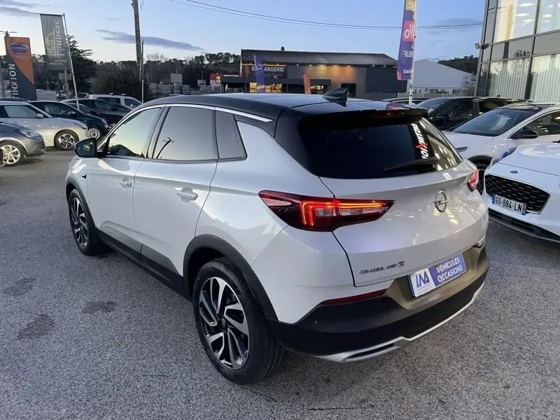 Opel Grandland X blanc avec toit noir, vue 3/4 arrière droit, feux arrière allumés, jantes alliage distinctives.