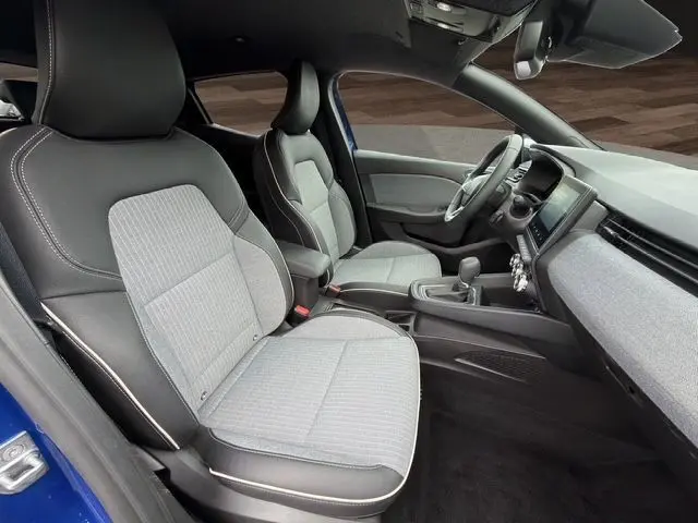 Intérieur avant de la Renault Clio V bleu Iron, vue côté gauche, sièges gris avec surpiqûres cuivre et tableau de bord moderne.
