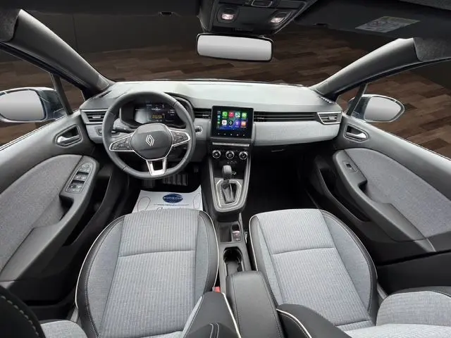 Vue intérieure avant de la Renault Clio V E-Tech hybride, sellerie grise avec surpiqûres cuivre et écran tactile central.