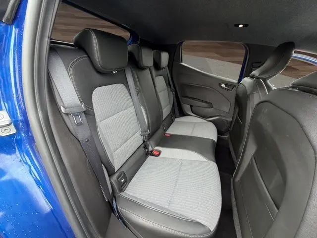 Vue intérieure arrière gauche de la Renault Clio V bleu Iron, montrant la banquette 3 places en textile gris/noir avec ceintures de sécurité.