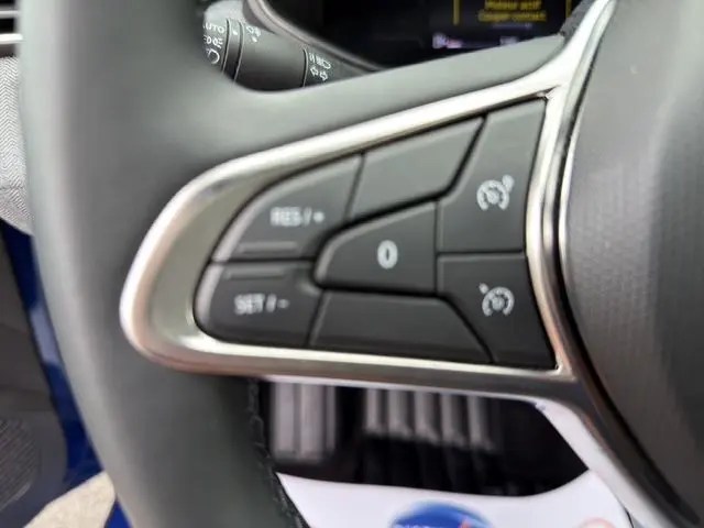 Gros plan sur les commandes de régulateur de vitesse au volant textile grainé de la Renault Clio V Bleu Iron.