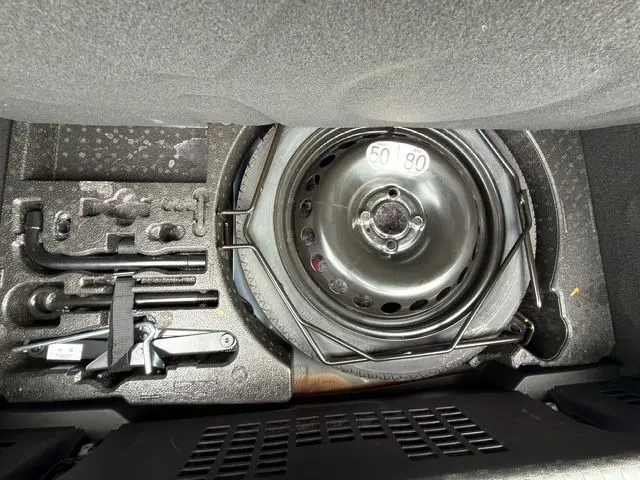 Gros plan sur la roue de secours et les outils de bord dans le coffre d'une Renault Clio V hybride bleu Iron.