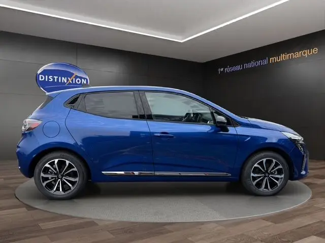 Profil côté gauche de la Renault Clio V E-Tech hybride bleu Iron avec jantes alliage et vitres arrière surteintées en showroom.