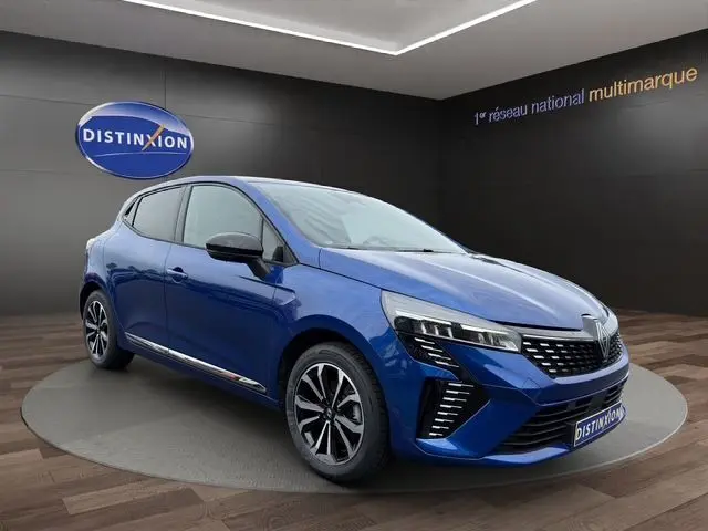 Renault Clio V E-Tech hybride bleu Iron en 3/4 avant droit, avec jantes alliage noires et calandre distinctive.