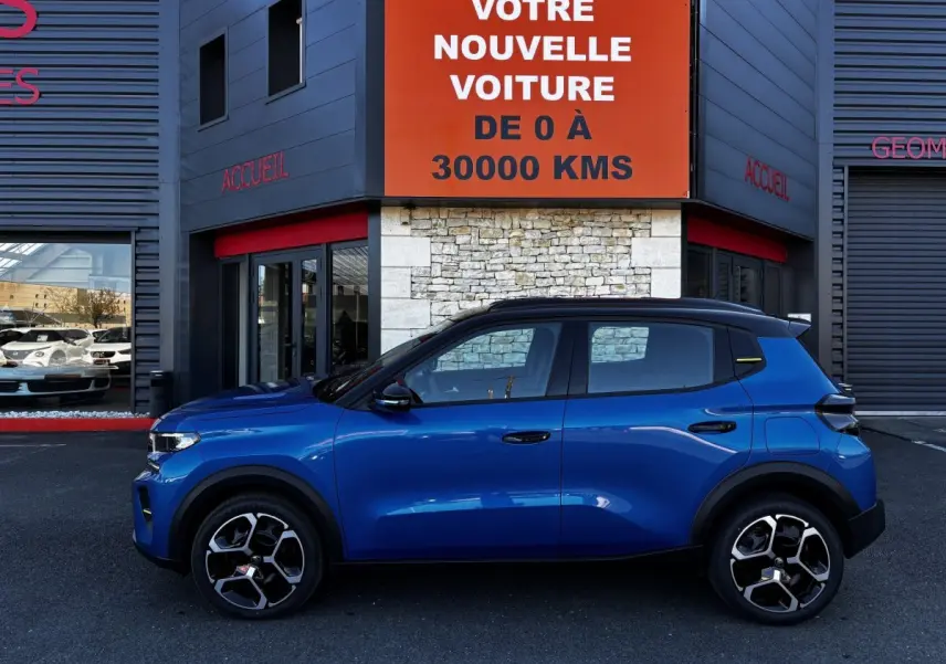 Profil côté gauche d'une Citroën C3 100 BVM PLUS bleu 2025 avec toit noir et jantes modernes, devant un bâtiment commercial.