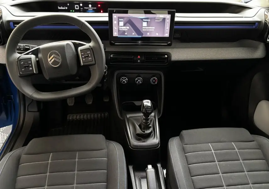 Vue intérieure avant de la Citroën C3 100 BVM PLUS 2025 bleue, avec volant cuir, écran tactile central et levier de vitesse manuel.
