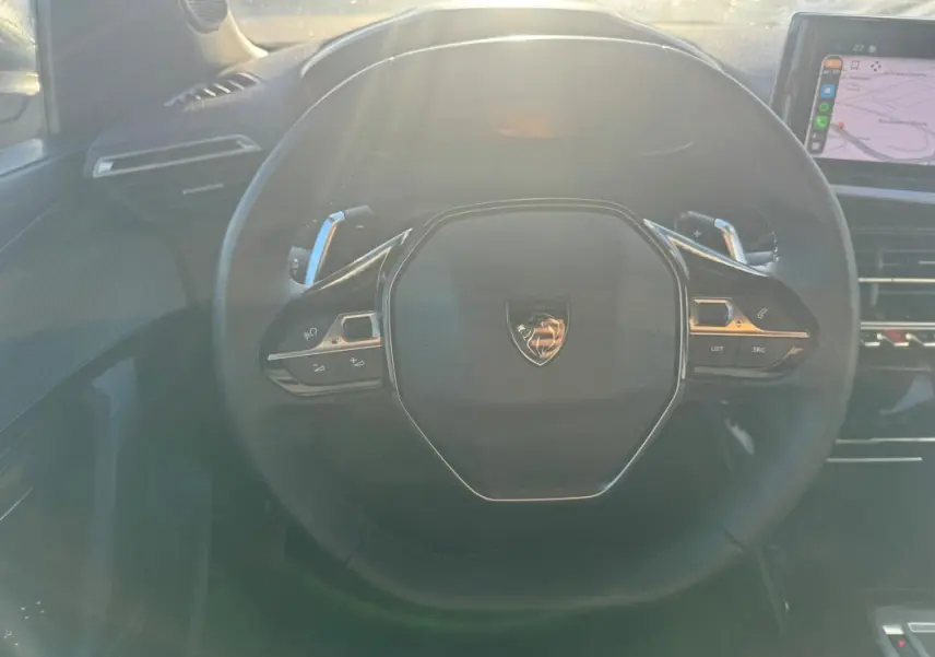 Vue rapprochée du volant noir du Peugeot 2008 Hybrid 136 e-DCS6 Allure 2024 avec commandes intégrées et écran tactile visible.