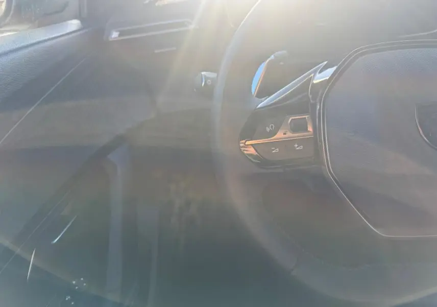 Vue partielle de l’intérieur du Peugeot 2008 Hybrid gris, avec le volant multifonction et commandes au volant visibles.