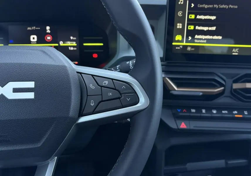 Vue rapprochée du volant et du tableau de bord digital du Dacia Duster gris, avec commandes au volant et écran tactile.