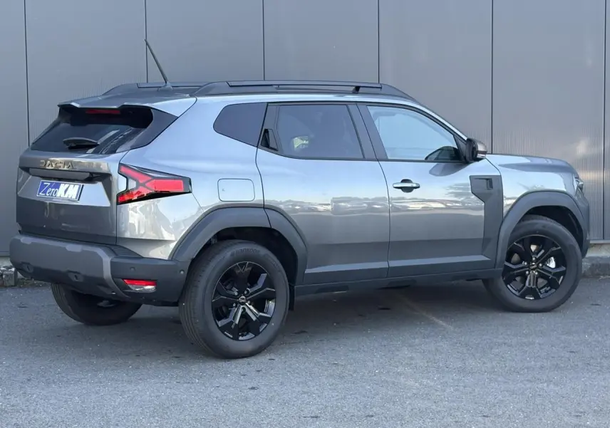 Vue latérale droite du Dacia Duster 2026 gris schiste avec jantes alliage noires et barres de toit longitudinales.