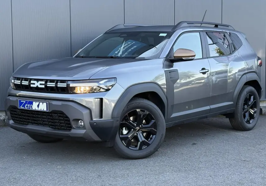 Vue 3/4 avant droit du Dacia Duster 2026 gris schiste avec jantes noires et barres de toit noires.