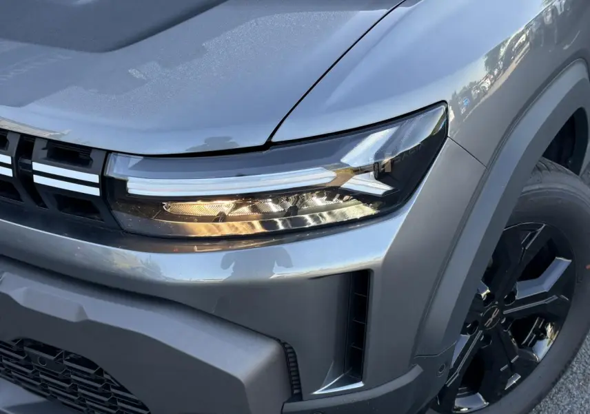 Gros plan sur l'avant droit du Dacia Duster gris schiste, mettant en valeur le phare LED et la jante alliage noire.