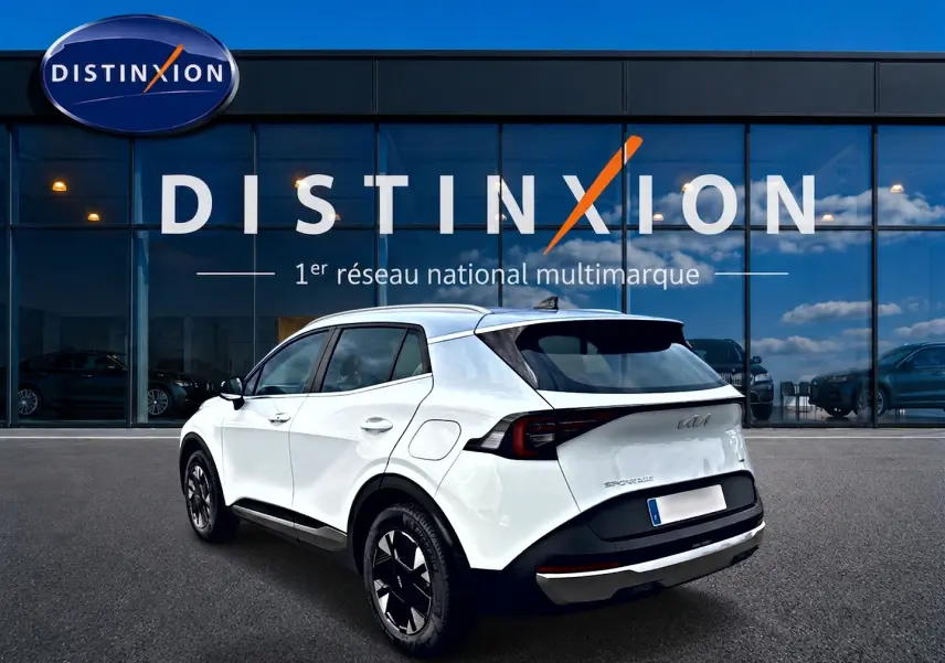 Vue 3/4 arrière droite d'un KIA Sportage blanc 2026 hybride, avec jantes alu noires et toit noir contrasté.