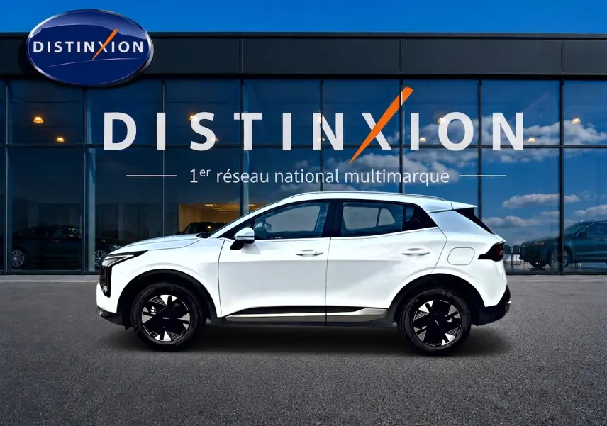 Vue latérale gauche d'un KIA Sportage blanc 2026 avec jantes alu noires et détails noirs contrastants.