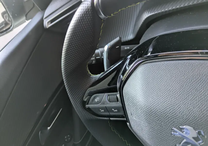 Gros plan sur le volant perforé avec surpiqûres jaunes du Peugeot 2008 GT blanc nacré, montrant les commandes intégrées.