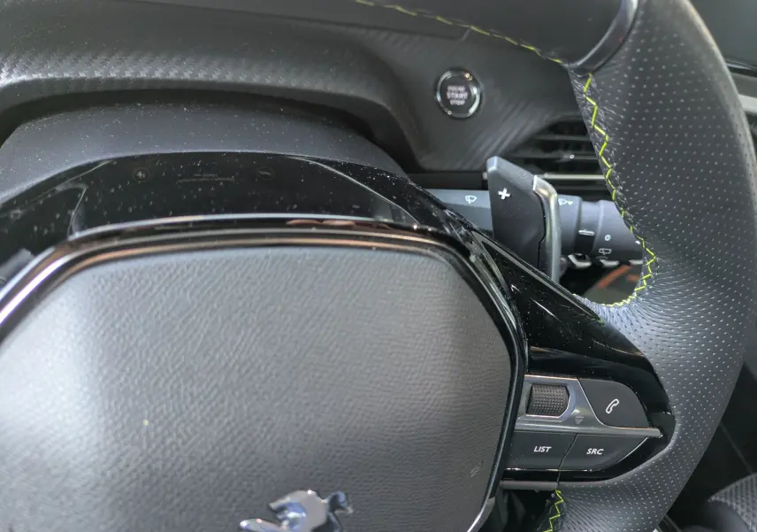 Gros plan sur le volant perforé avec surpiqûres vertes et commandes intégrées du Peugeot 2008 GT blanc nacré, tableau de bord en arrière-plan.