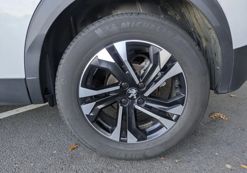 Gros plan sur la roue avant gauche d’un Peugeot 2008 blanc nacré avec jante alliage noire et argentée.