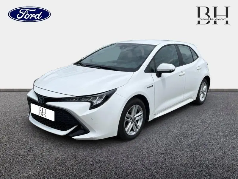 Toyota Corolla 184h Dynamic Business blanc pur vue 3/4 avant droit avec calandre noire et jantes alu.