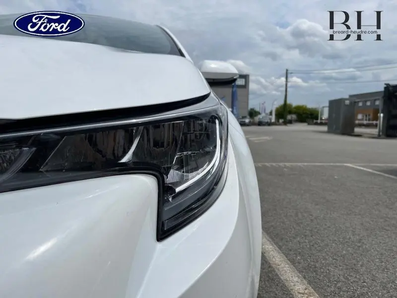 Gros plan sur le phare avant droit blanc pur d'une Toyota Corolla 184h Dynamic Business, avec carrosserie lisse et moderne.