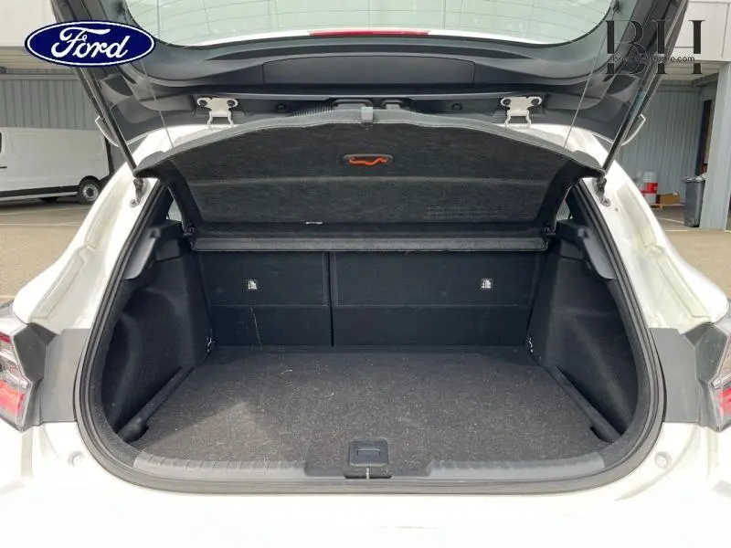 Coffre ouvert vu de l'arrière d'une Toyota Corolla blanche, montrant l'espace de chargement vide et la trappe de couverture.