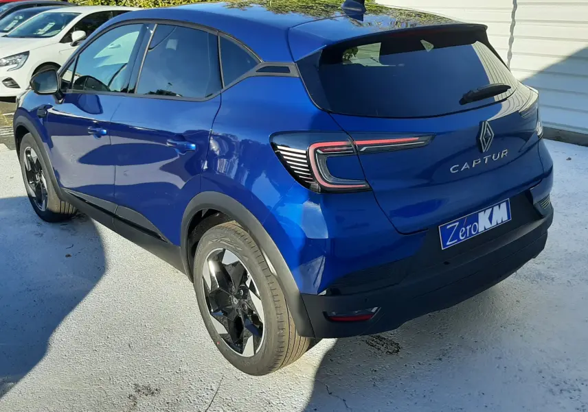 Vue 3/4 arrière droite d'un Renault Captur bleu Iron 2025 avec feux arrière LED et jantes noires biton.