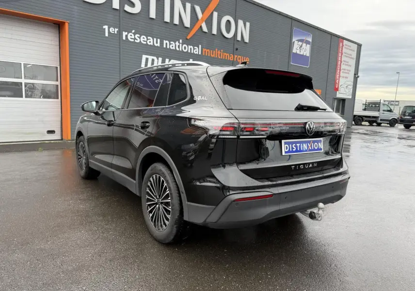 Volkswagen Tiguan noir grenadille métallisé vu en 3/4 arrière droit avec crochet d'attelage et jantes alliage 18 pouces.