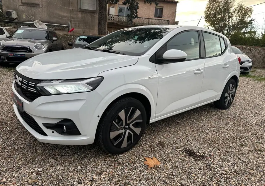 Dacia Sandero TCe 90 blanc vue 3/4 avant droit, avec phares allumés et jantes au design moderne.