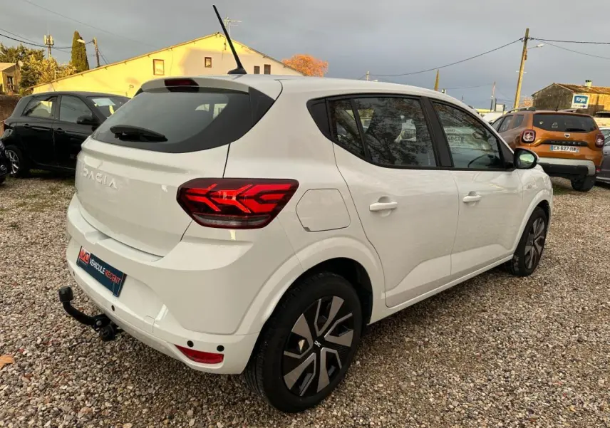 Vue 3/4 arrière droite d'une Dacia Sandero blanche 2024 avec feux arrière LED et attelage de remorque.